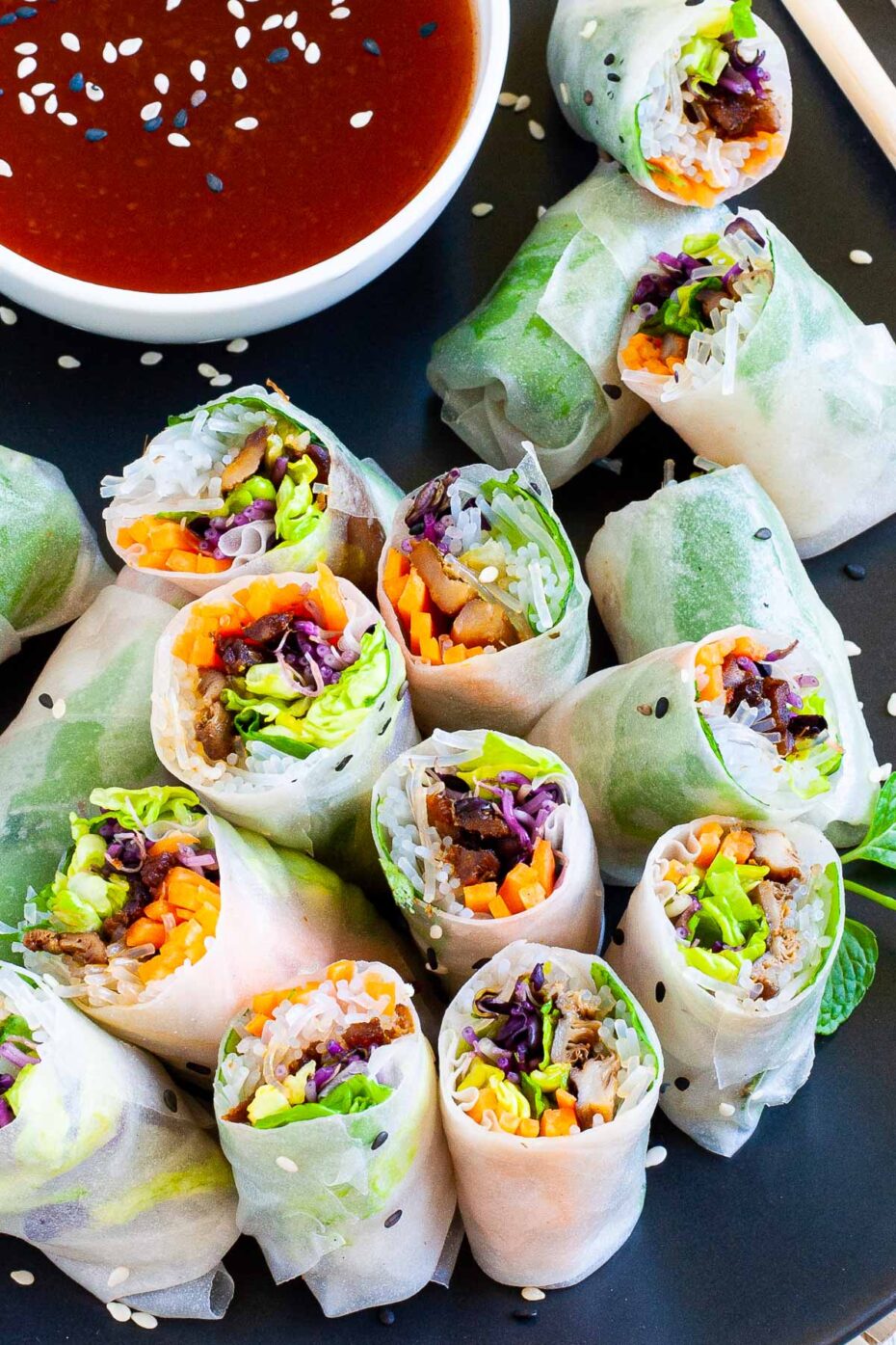 Fresh rice paper rolls are cut in half and arranged on a black plate. The colorful filling is visible purple sprouts, shredded carrot, lettuce, vermicelli noodles and brown mushroom