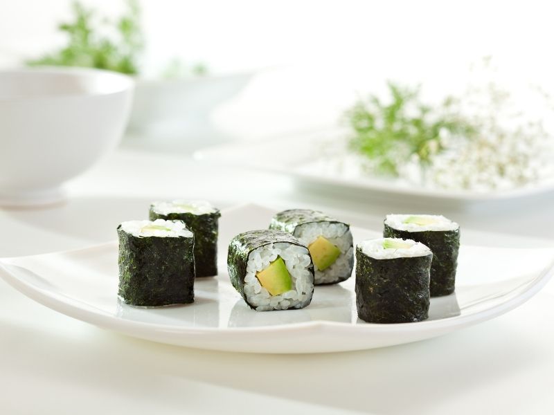 6 rolled sushi filled with avocado slices and rice wrapped in nori sheets