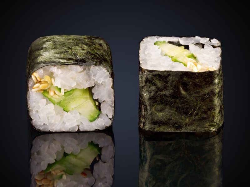 2 sushi rolls filled with green vegetables around rice and nori sheets
