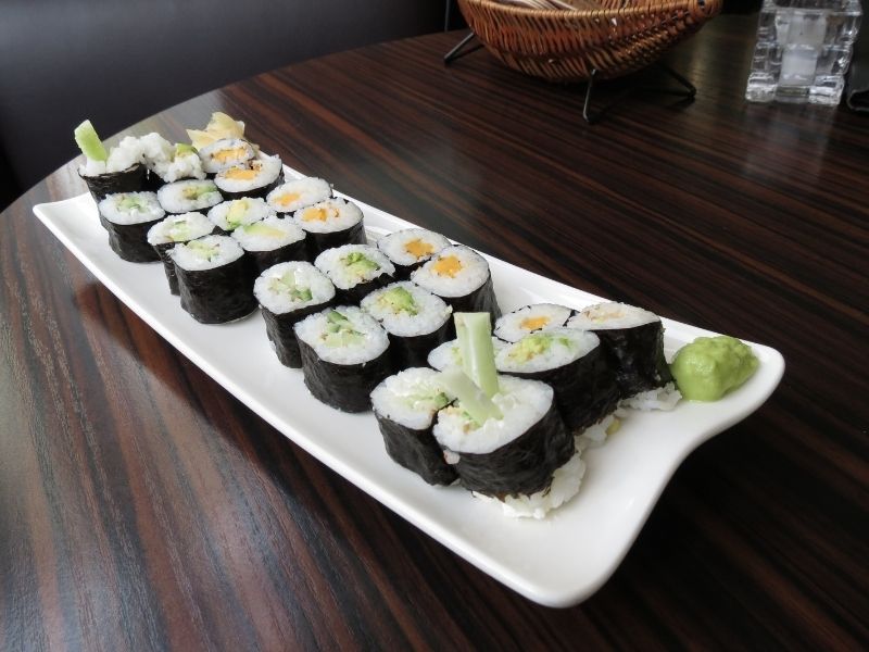 Long white plate with several sushi rolls with different fillings wrapped in seaweed sheets