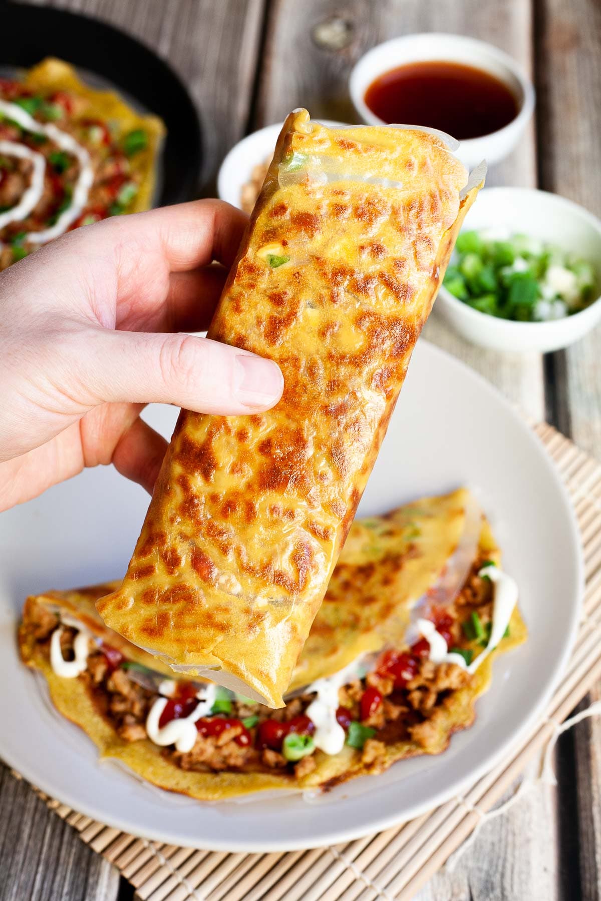 A hand is holding a folded rice paper pizza with yellow and brown spots