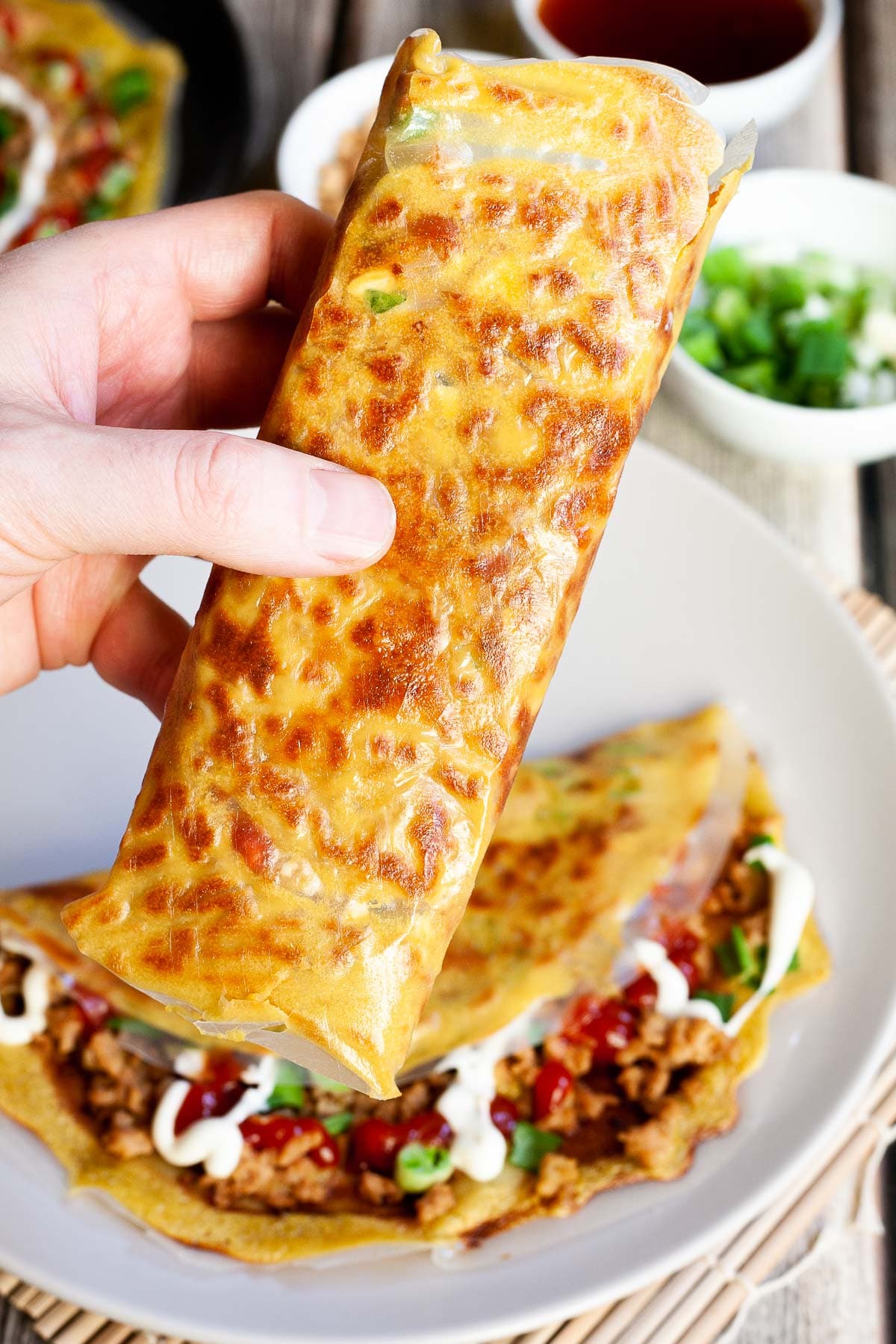 A hand is holding a folded rice paper pizza with yellow and brown spots