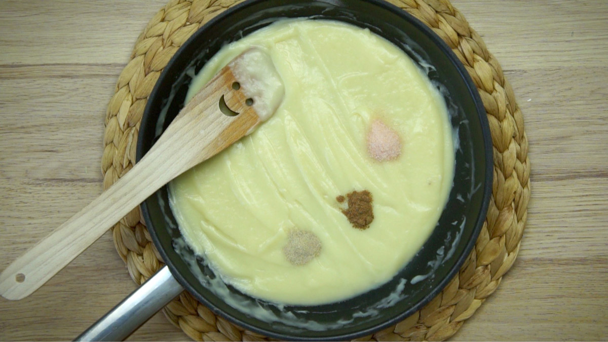 Frying pan with light yellow sauce and small heaps of nutmeg, salt, and garlic powder.