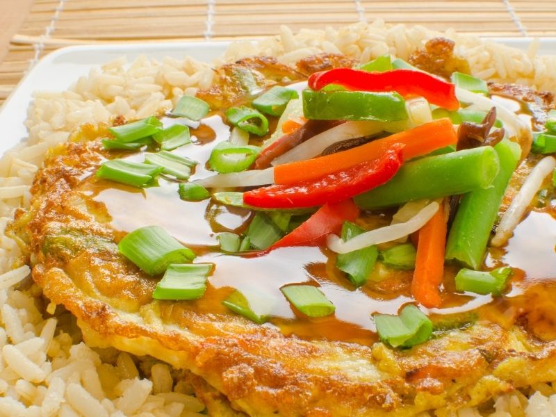 Egg omelette served on rice and topped with slices bell peppers and spring onion rings. 