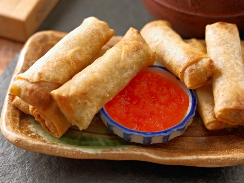 Crispy bubbly egg rolls in a plate with a red dipping sauce in the middle