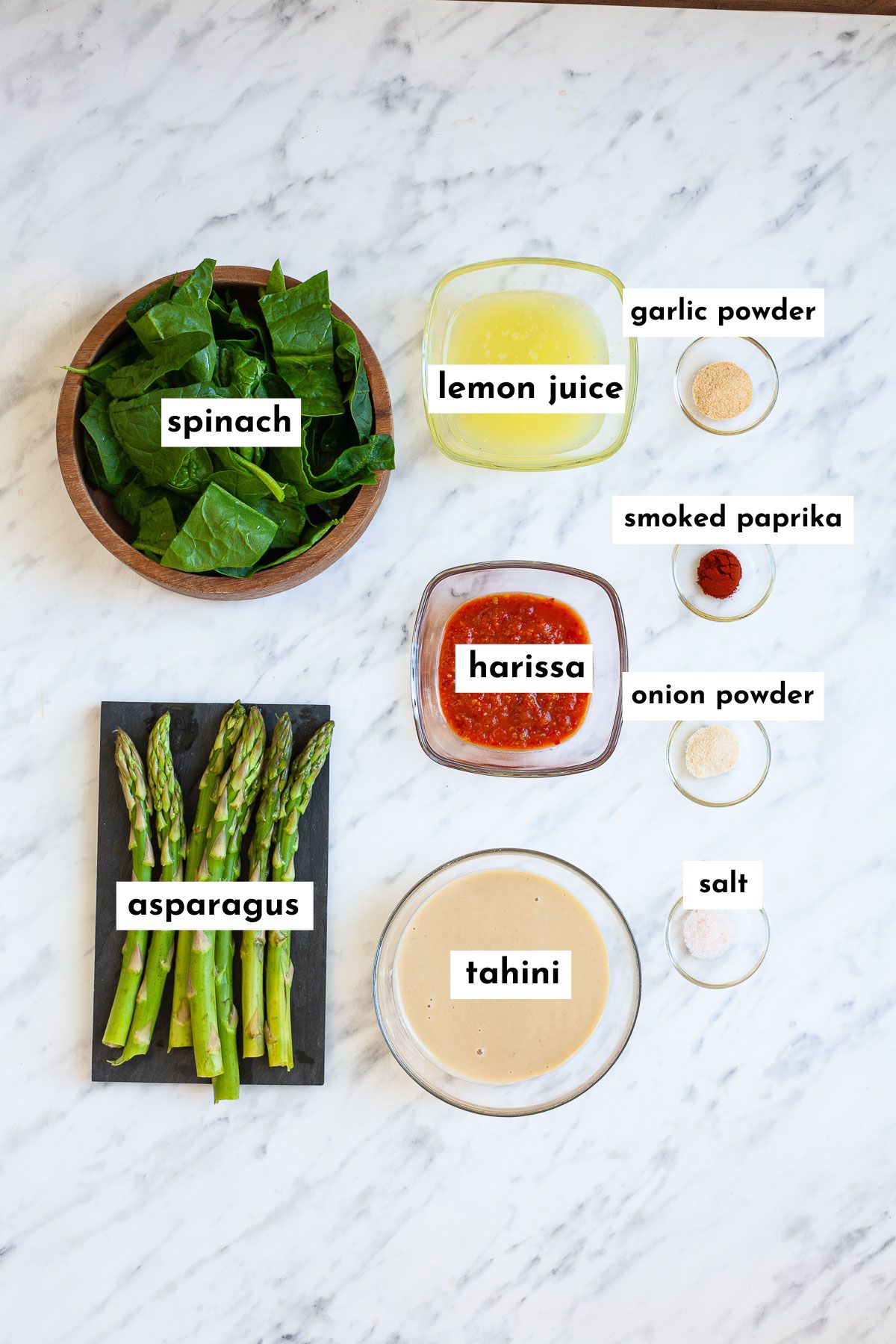 Ingredients of this harissa tahini pasta sauce measured in small glass bowls like spinach leaves, asparagus, harissa paste, tahini, lemon juice, garlic powder, paprika powder, onion powder and salt