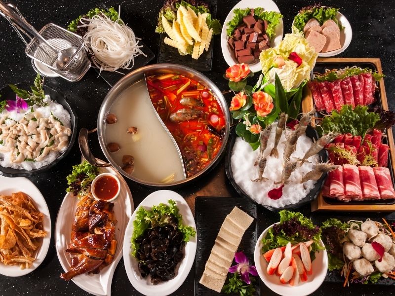 Various colorful meals in small white plates around a two sections hot pot pan. 