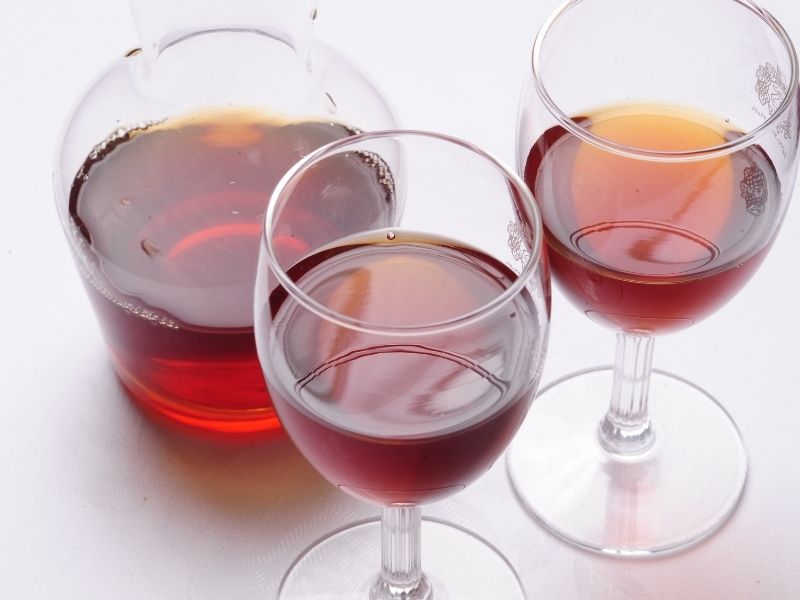 Two tall glasses with red liquid and a decanter with red liquid