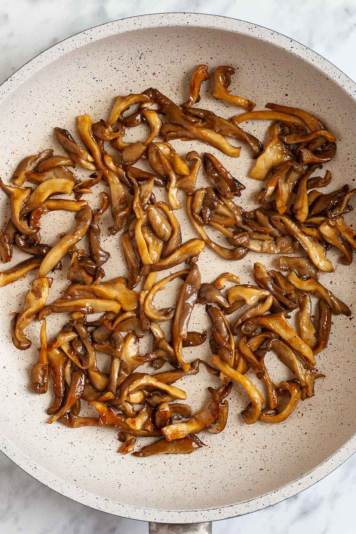 White frying pan with brown glazed mushroom slices