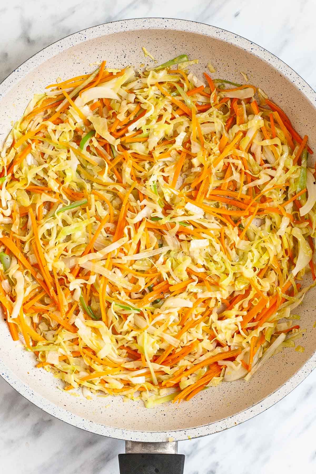 White frying pan with shredded orange, green and white vegetables.