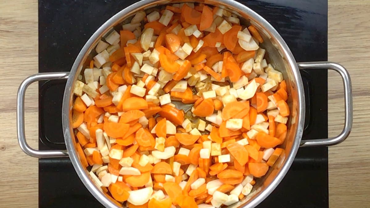 Large pot with lots of chopped orange and white veggies like carrot, celeriac and parsnip.