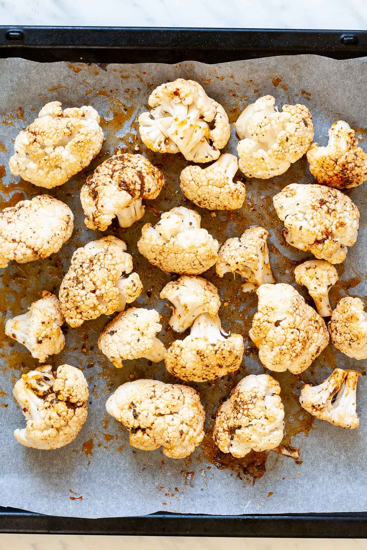 Cauliflower florets drizzled with a brown spicy marinade is spread out in one layer on a sheet pan