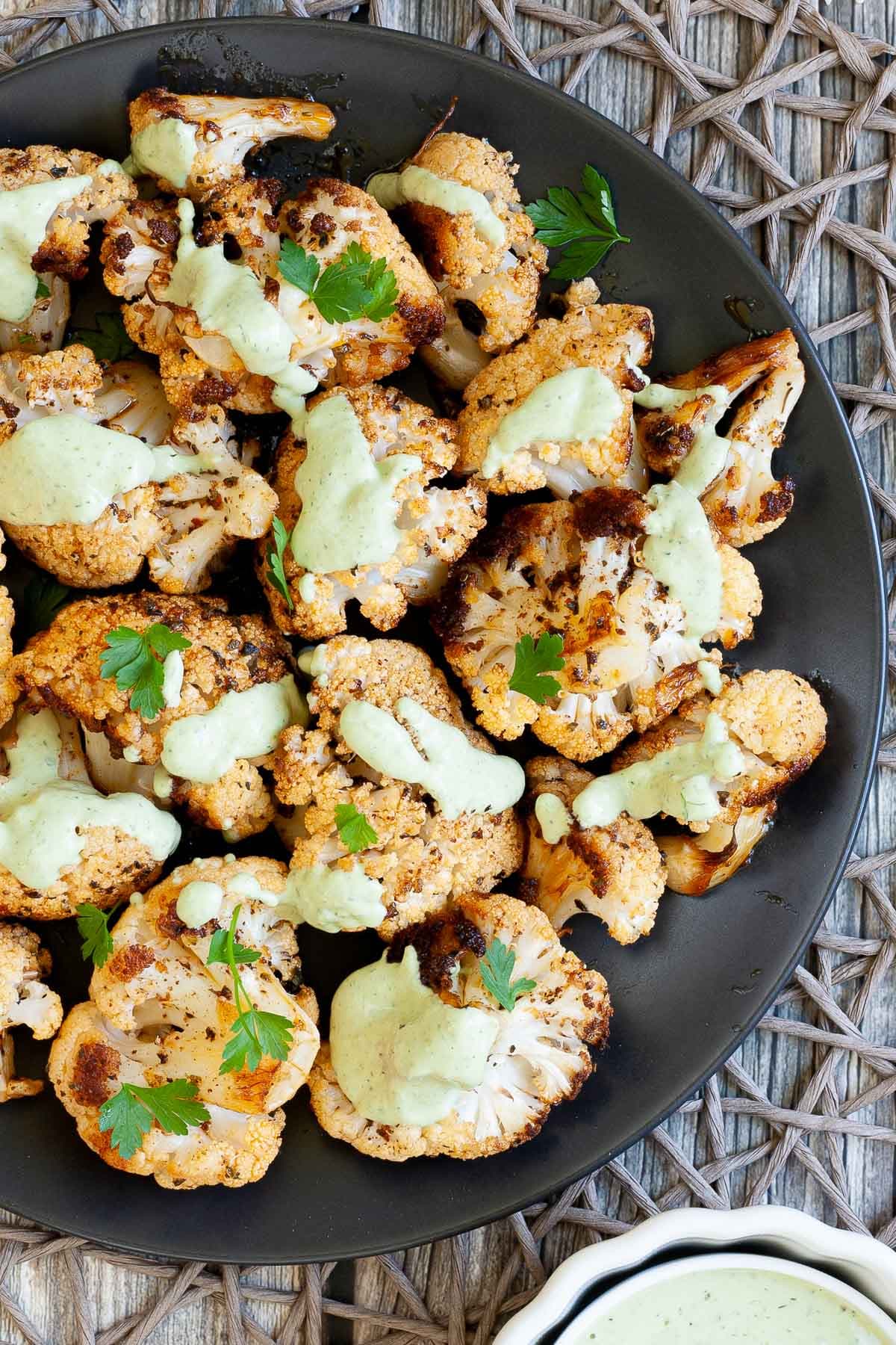 Black plate full of roasted cauliflower florets drizzled with a light green creamy sauce and sprinkled with fresh parsley