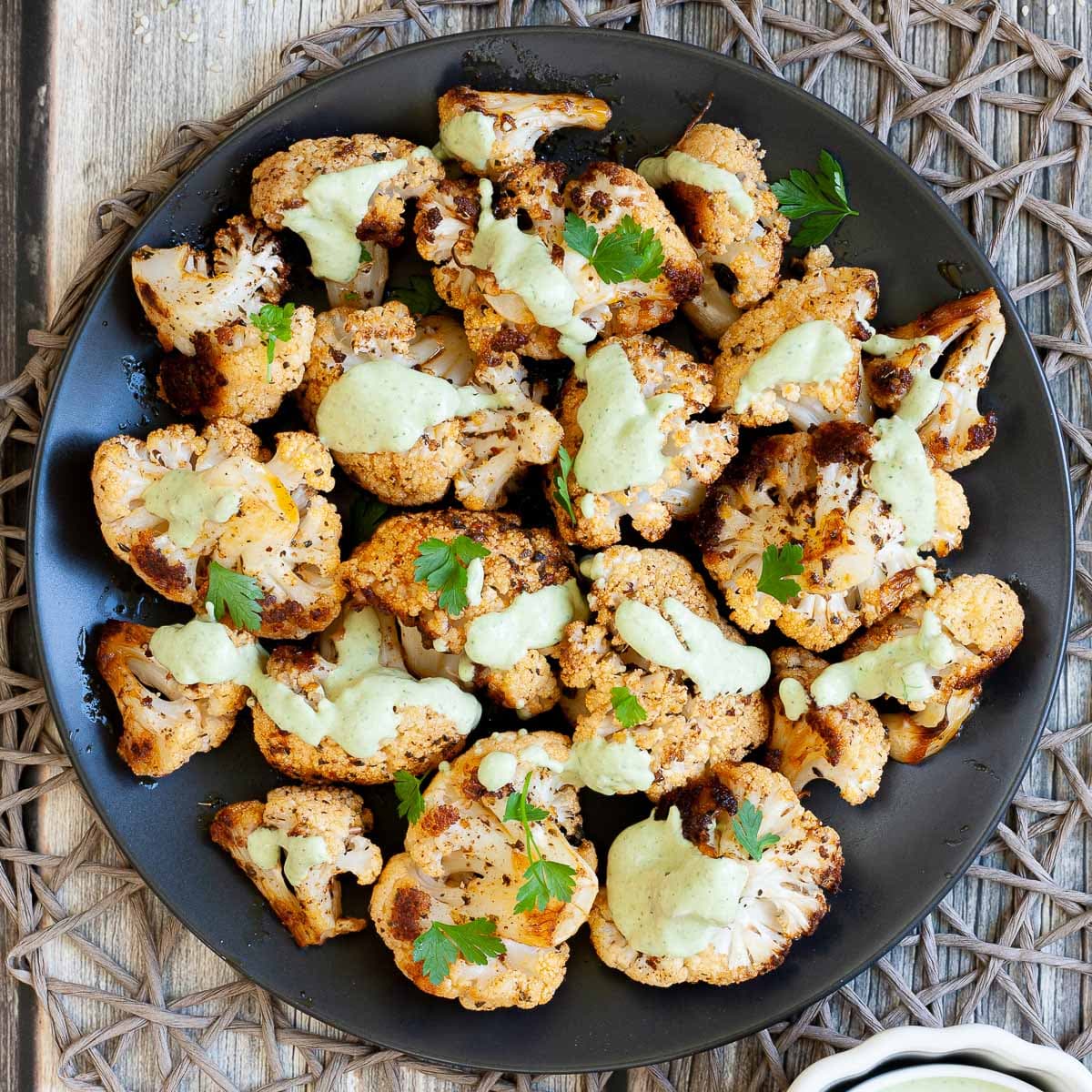 Black plate full of roasted cauliflower florets drizzled with a light green creamy sauce and sprinkled with fresh parsley