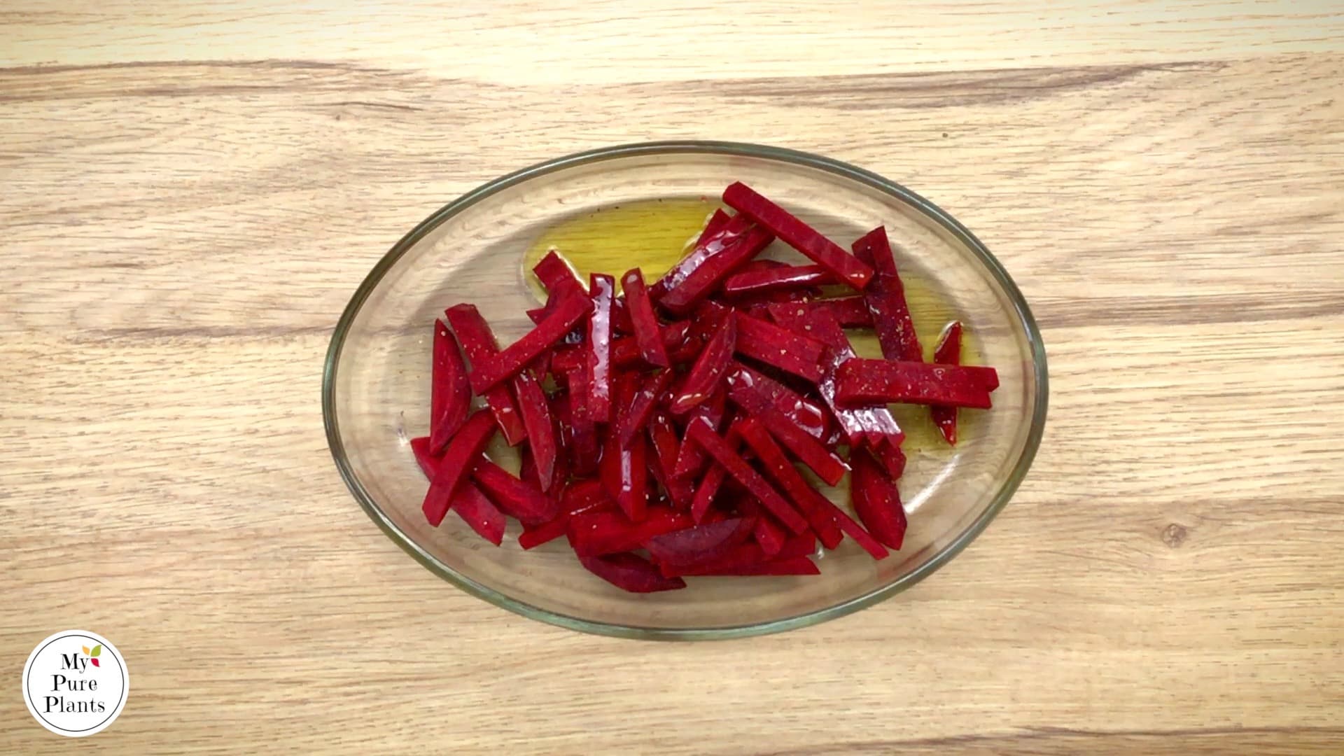 Raw beet sticks drizzled with oil, salt, and black pepper in a large glass bowl.