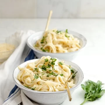 2 bowls of pasta dish with white sauce sprinkled with chopped herbs.
