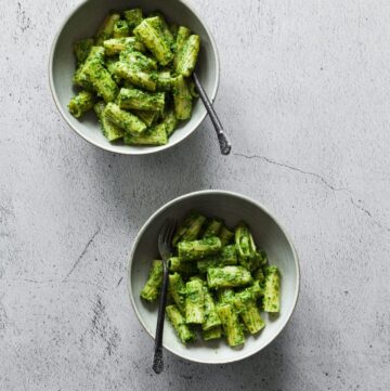 Two small white bowl with penne in a green pesto sauce