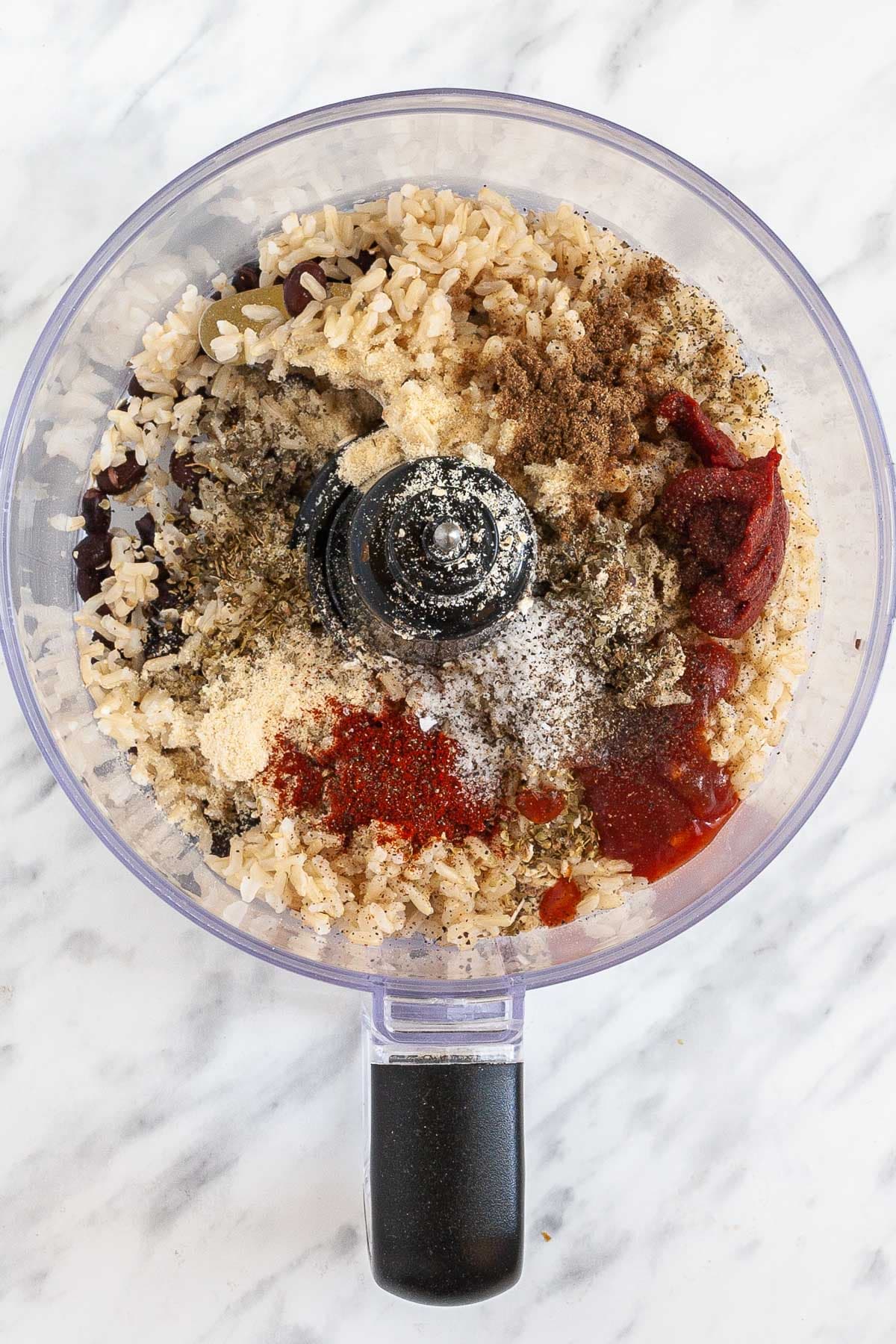 A food processor with the ingredients of this chipotle black bean burger. Rice, tomato paste, black beans and other spices are visible.
