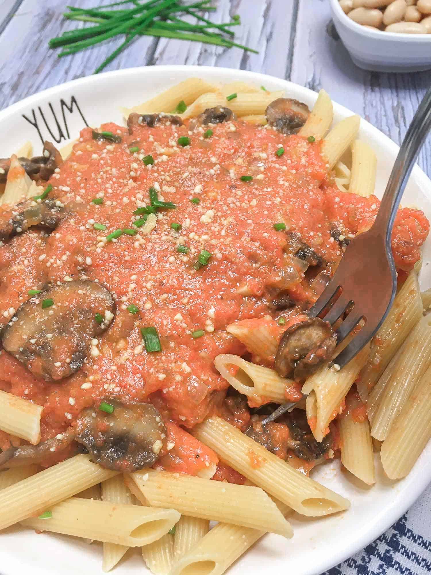 Penne pasta topped with a light red sauce with mushrooms springkled with yellow flakes and chopped herbs
