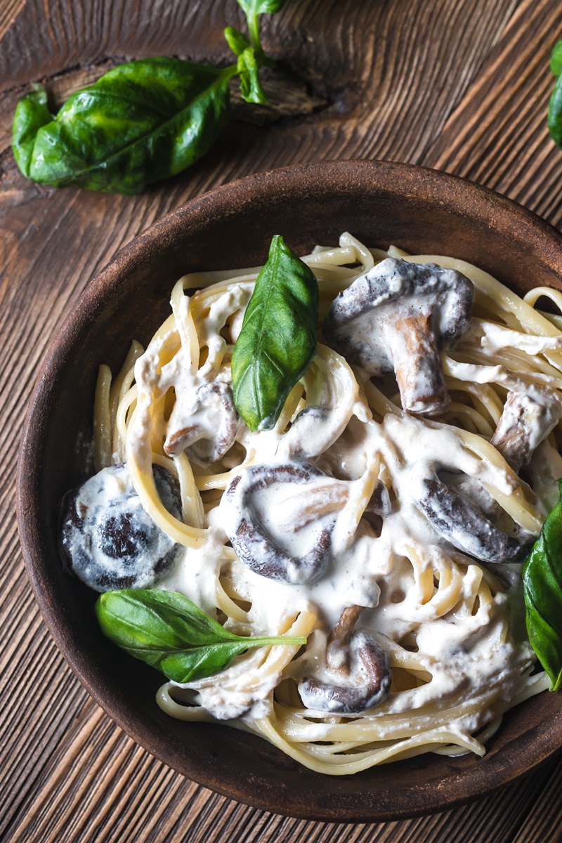 Brown wooden bowl with tagliatelle, mushroom slices, basil leaves in white sauce