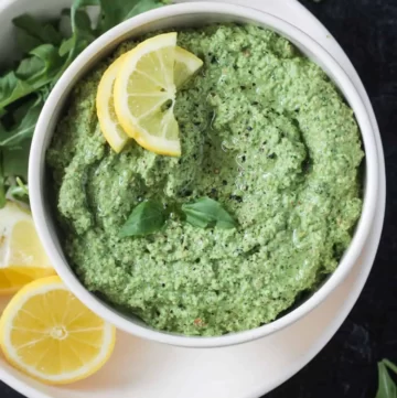 Green pesto sauce in a small bowl topped with lemon slices