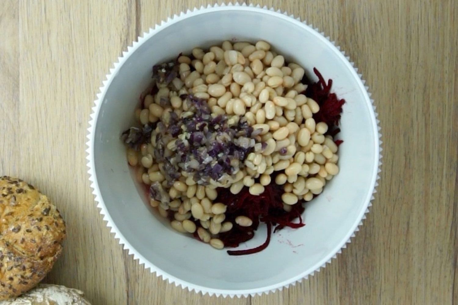 White mixing bowl is grated purple beets, oats, white beans, chopped red onion and garlic. 