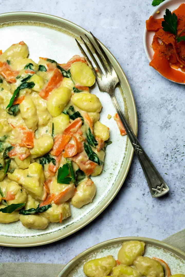 White plate with gnocchi in a white sauce as well as spinach leaves and fake salmon slices