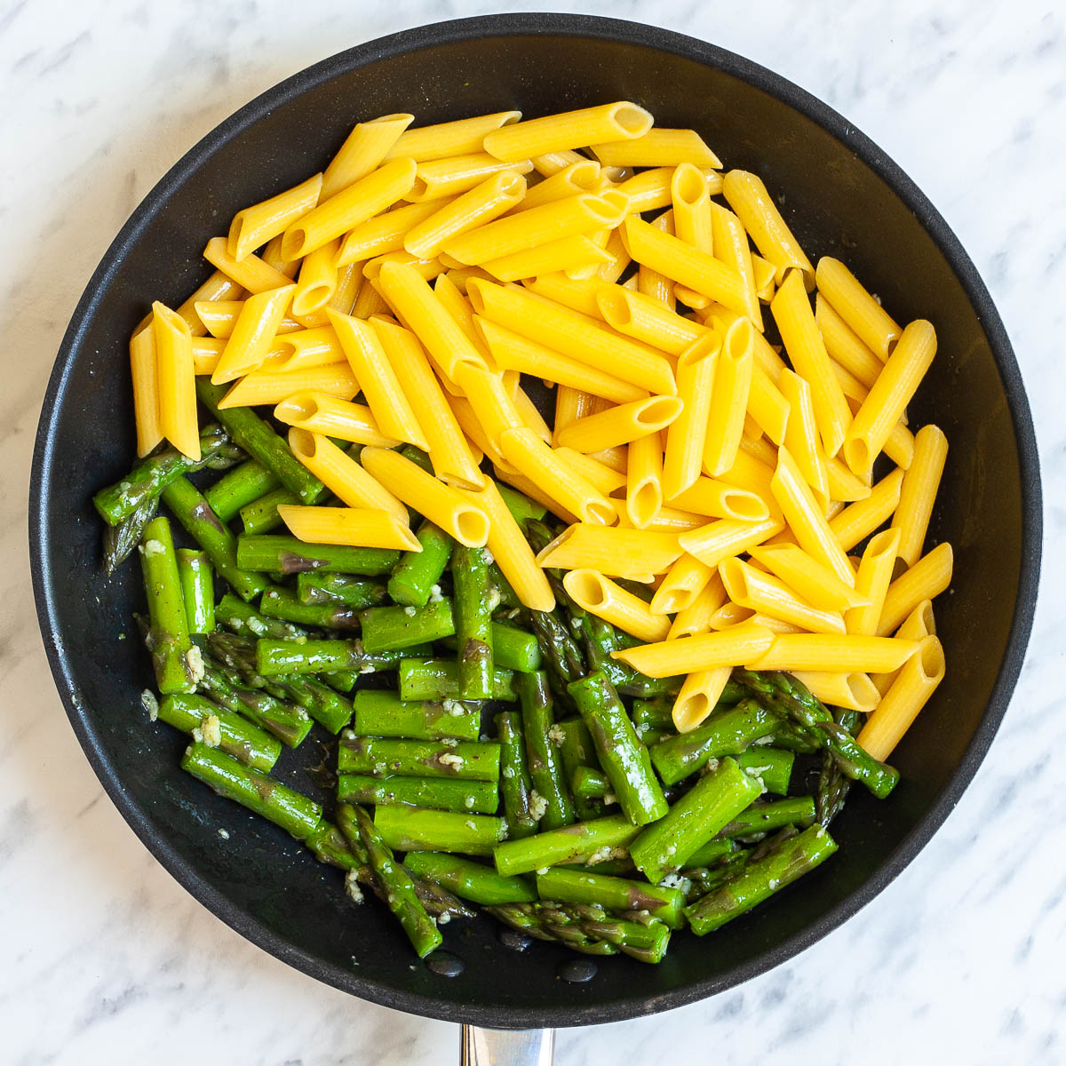 Black frying pan with penne pasta and asparagus.