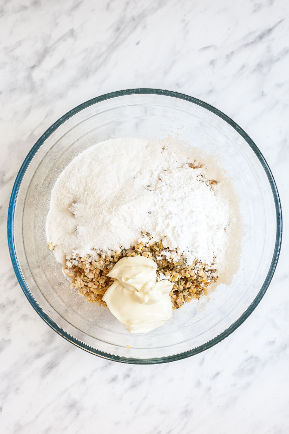 A glass bowl with flour, mayo, and light brown crumbles. 