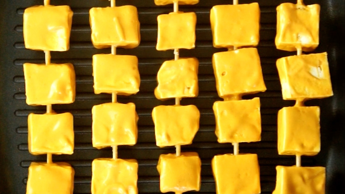 Tofu cubes covered in thick orange marinade on skewers.
