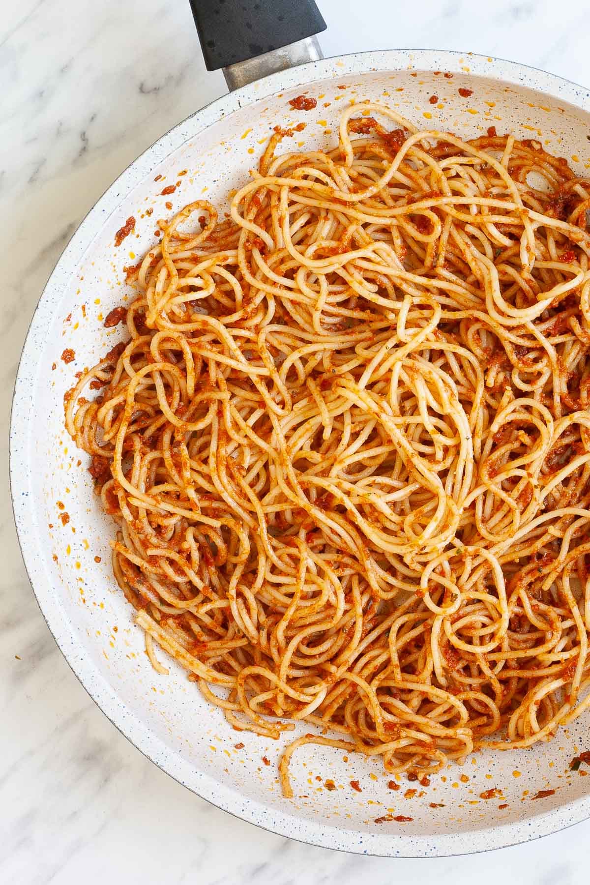 Red pesto spaghetti in a white frying pan