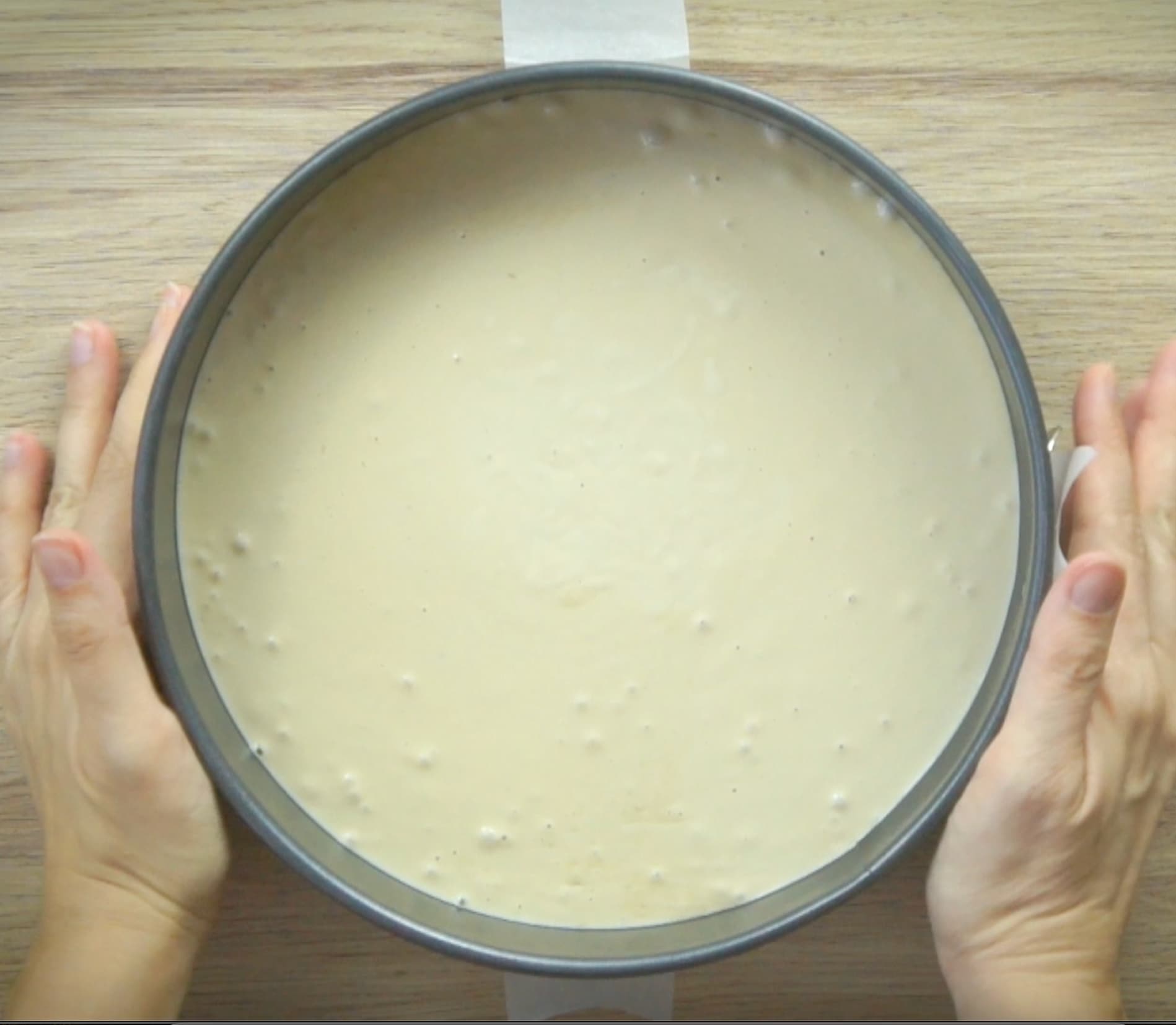 Two hands are holding acake pan with yellow batter.