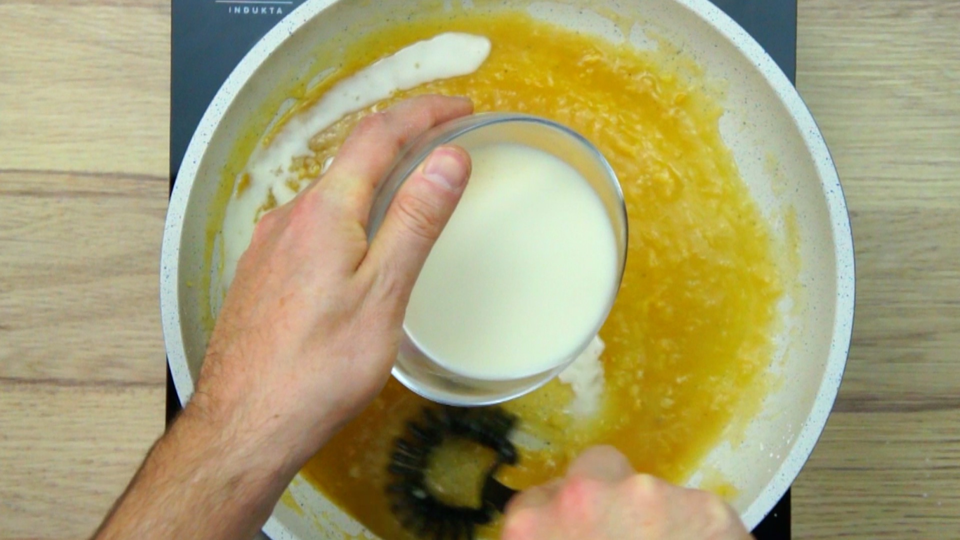 A hand is adding white liquid to the yellow liquid.