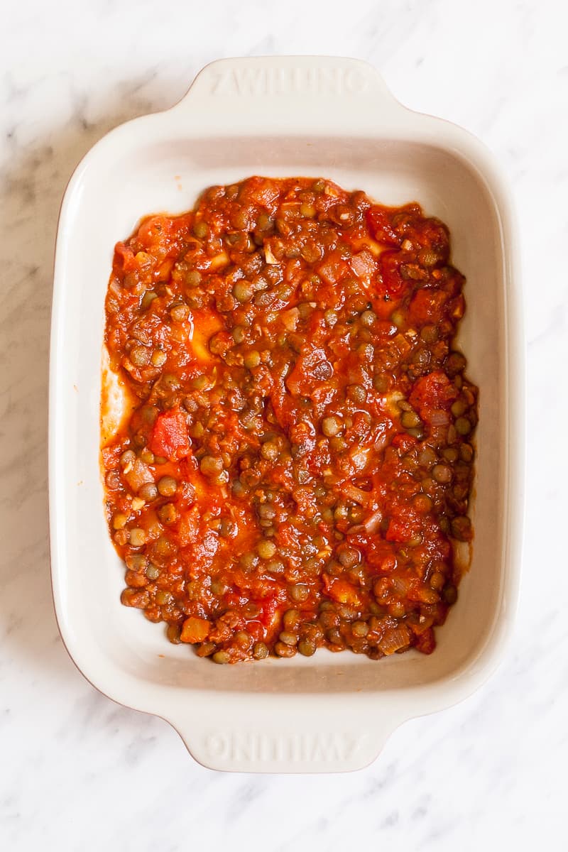 Lentils in red sauce in the bottom of an oven-safe dish.