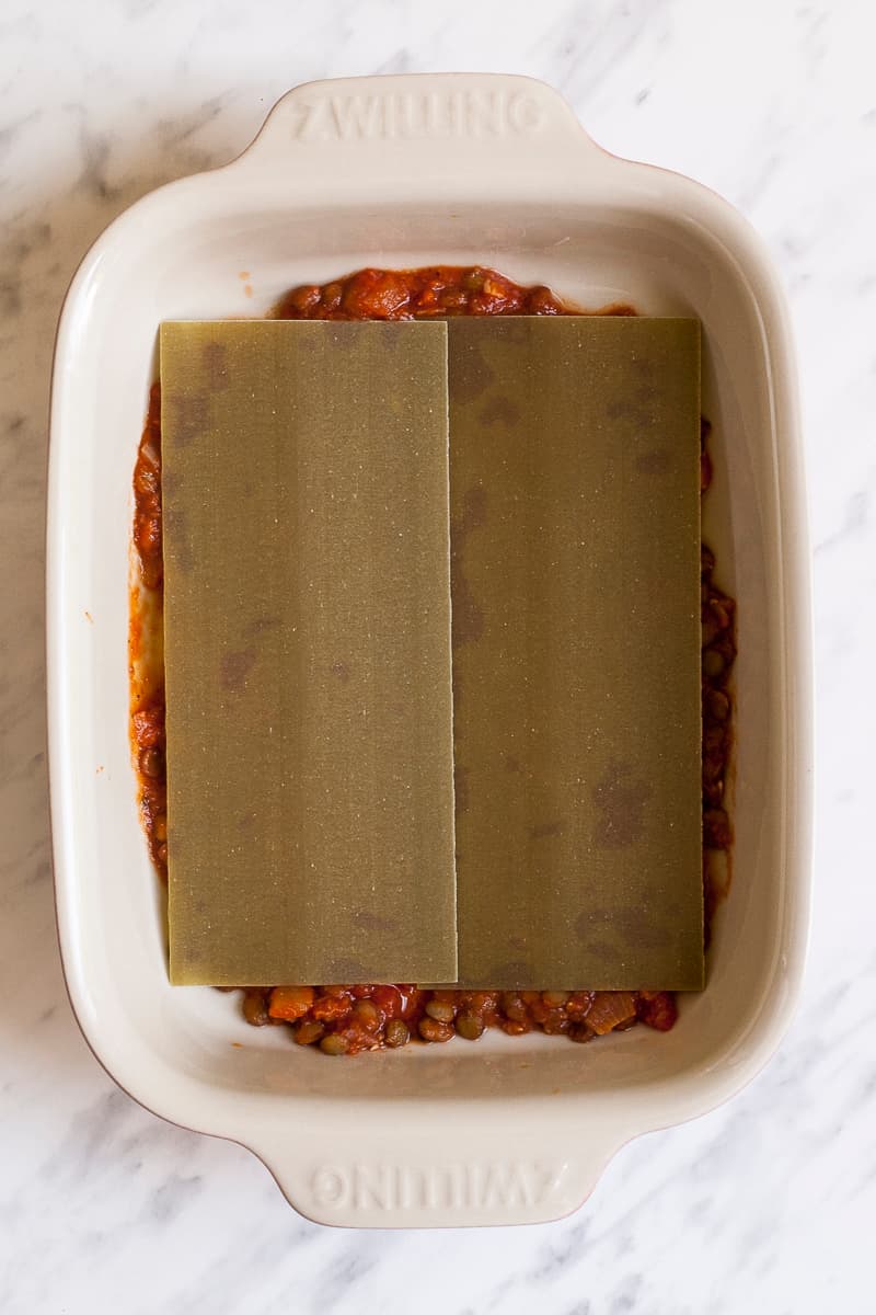 Lentils in red sauce covered with a pasta sheet in the bottom of an oven-safe dish.