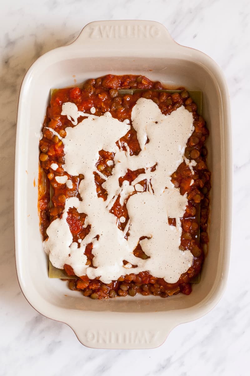 Pasta sheets are covered with lentils in red sauce and white sauce.