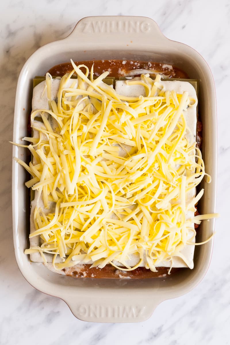 Oven-safe dish with red sauce, pasta sheets and shredded cheese on top.