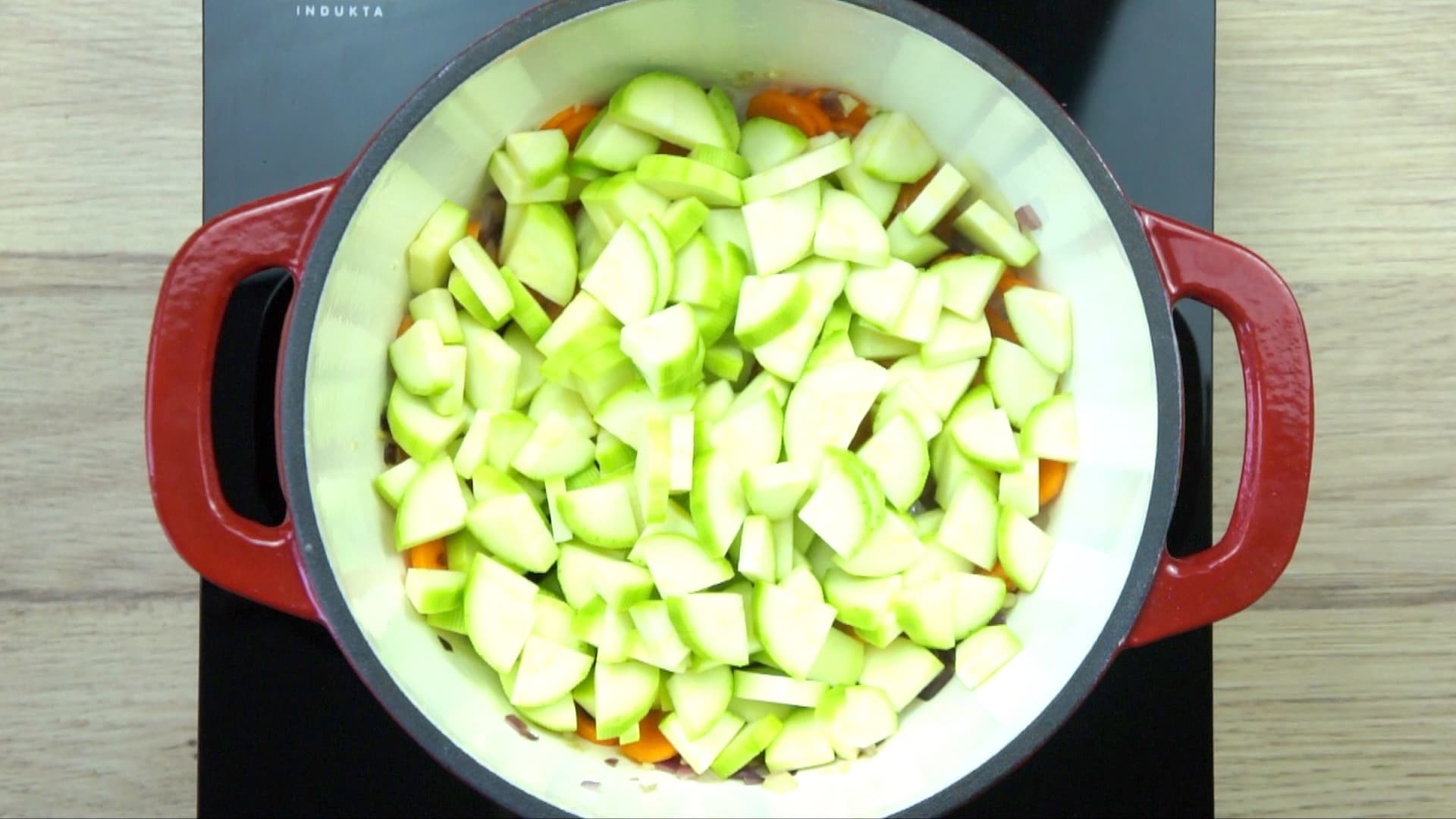 Chopped onion, garlic, zucchini, and sliced carrots in a white red enamelled Dutch oven.