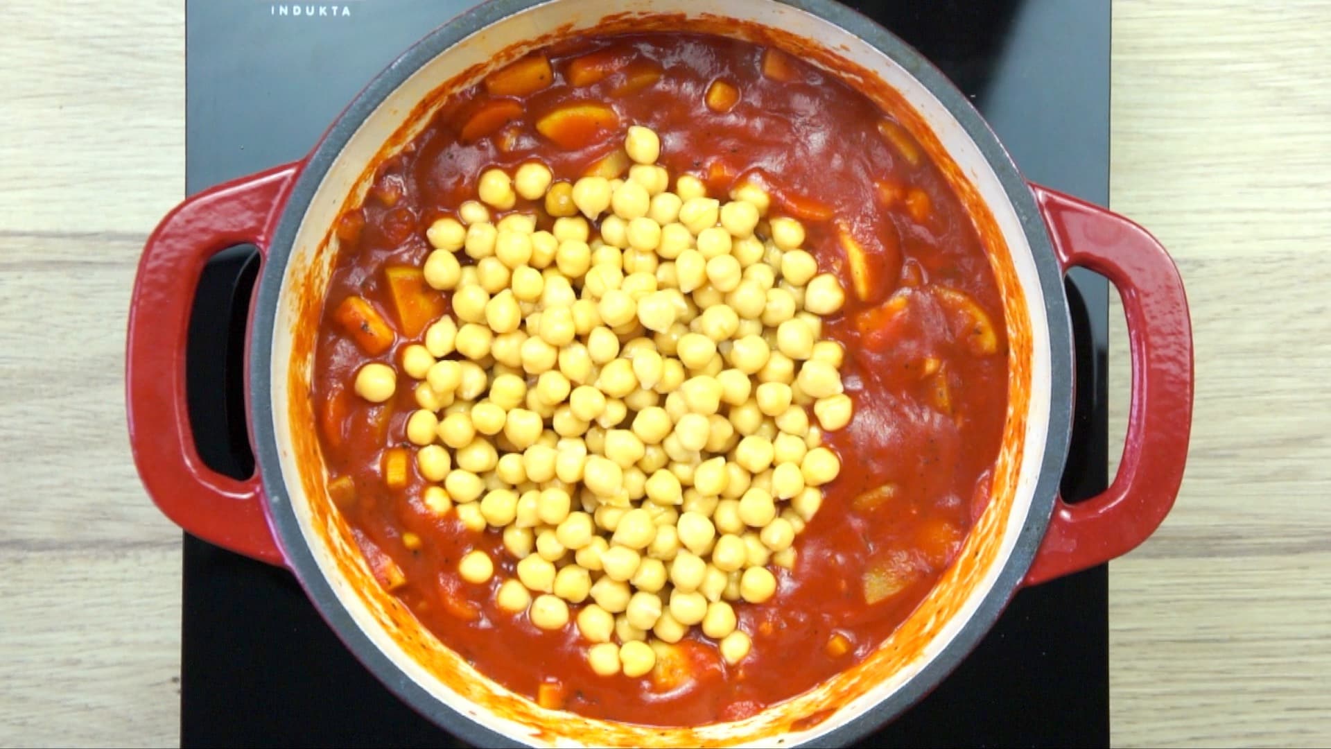 Veggie chunks covered with red tomato sauce and a large heap of chickpeas in a white red enamelled Dutch oven.