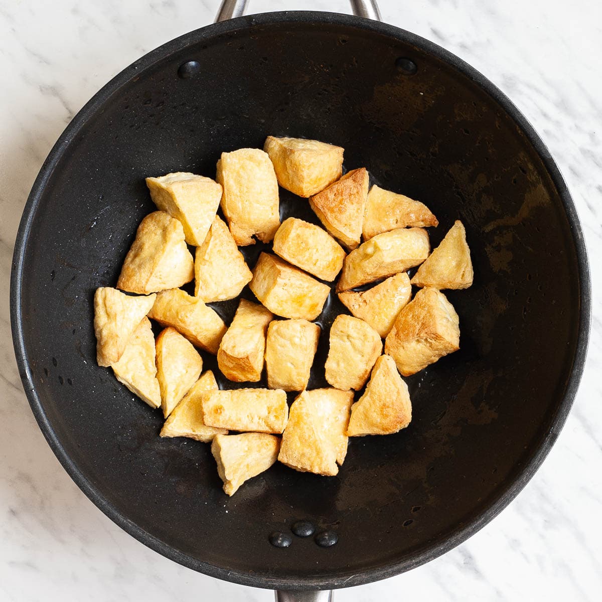 Puffy light brown triangle shaped tofu cubes in a large wok.