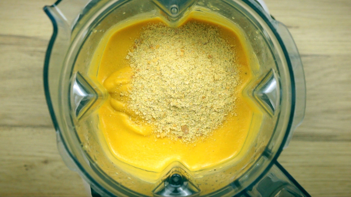 Blender with thick orange sauce with a heap of yellow flakes on top.