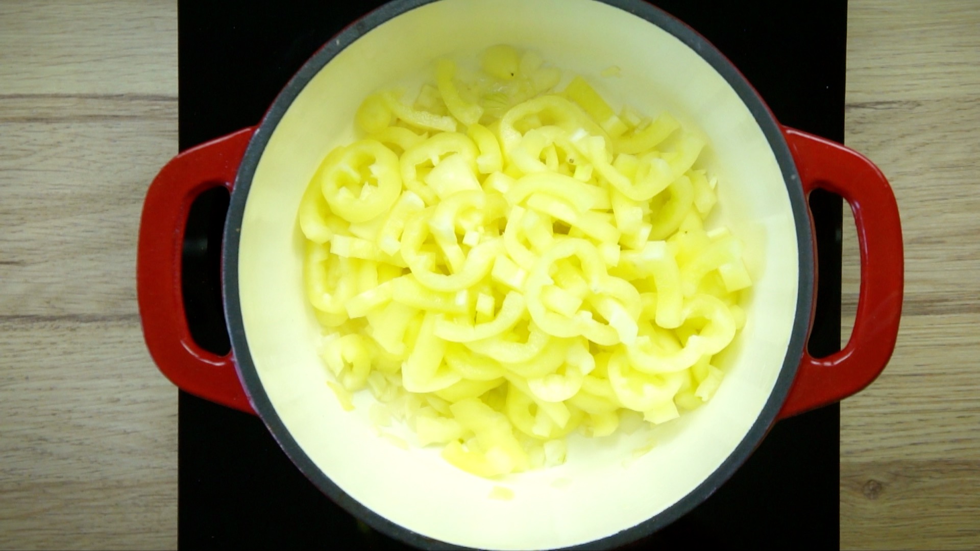 Yellow pepper slices in a white red enameled Dutch oven. 