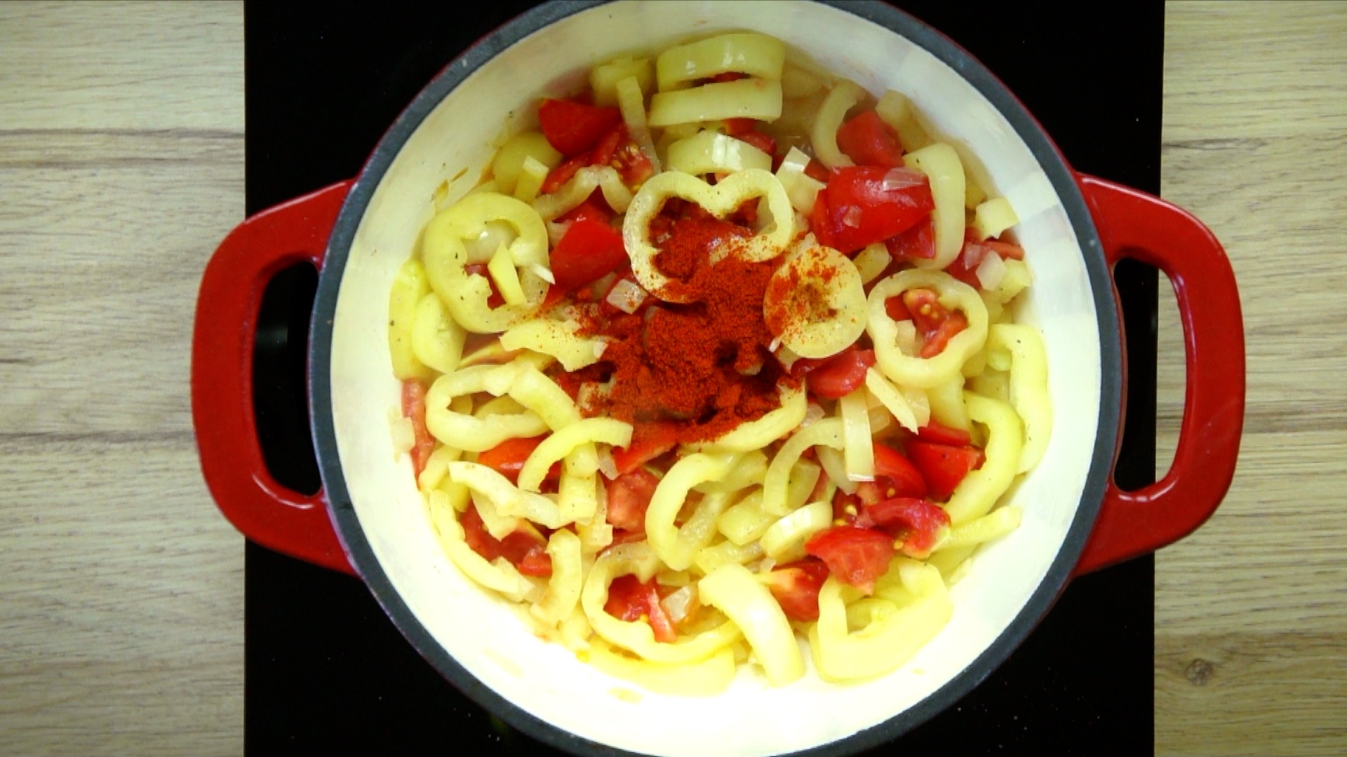 Yellow pepper and tomato slices with heaps of red paprika powder in a white red enameled Dutch oven.