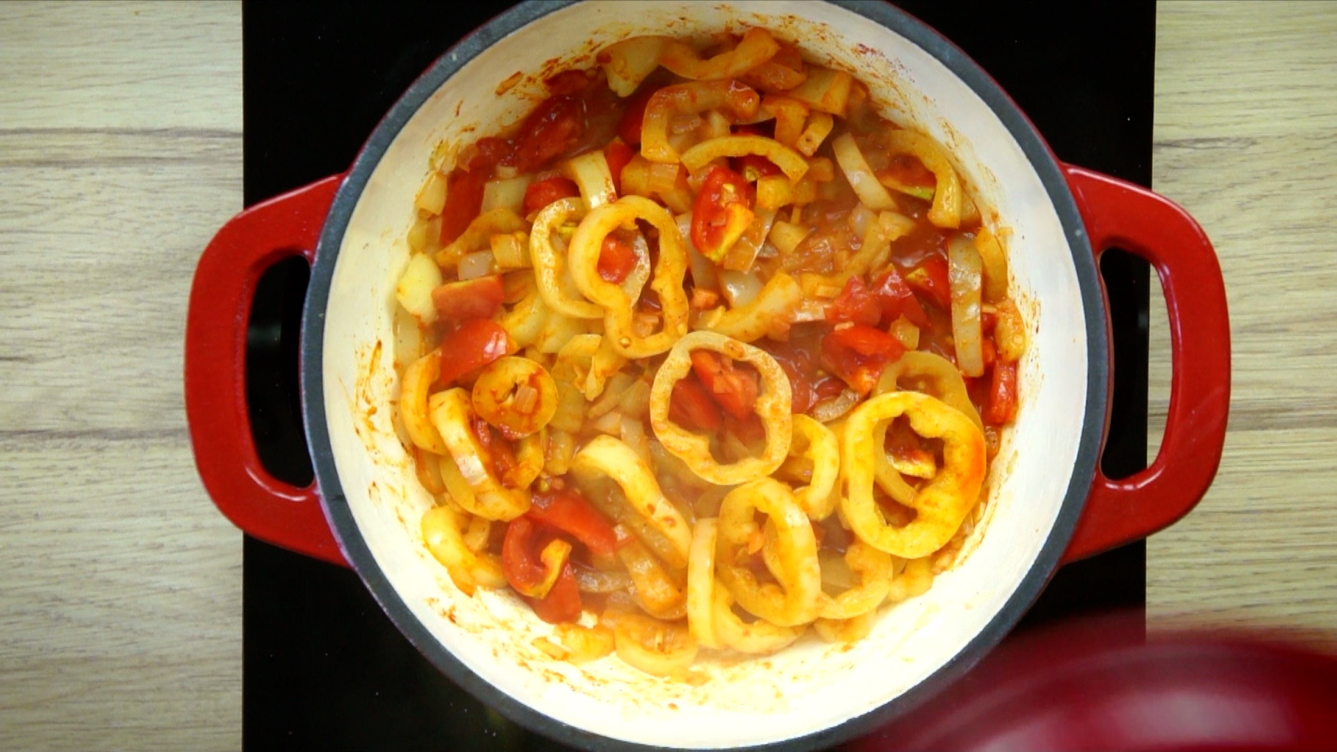 Yellow pepper and tomato slices in orange liquid in a white red enameled Dutch oven.