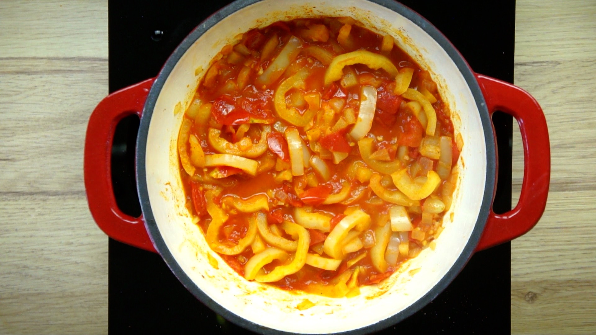 Soften yellow pepper and tomato slices are about to create a juicy stew in a white red enameled Dutch oven.