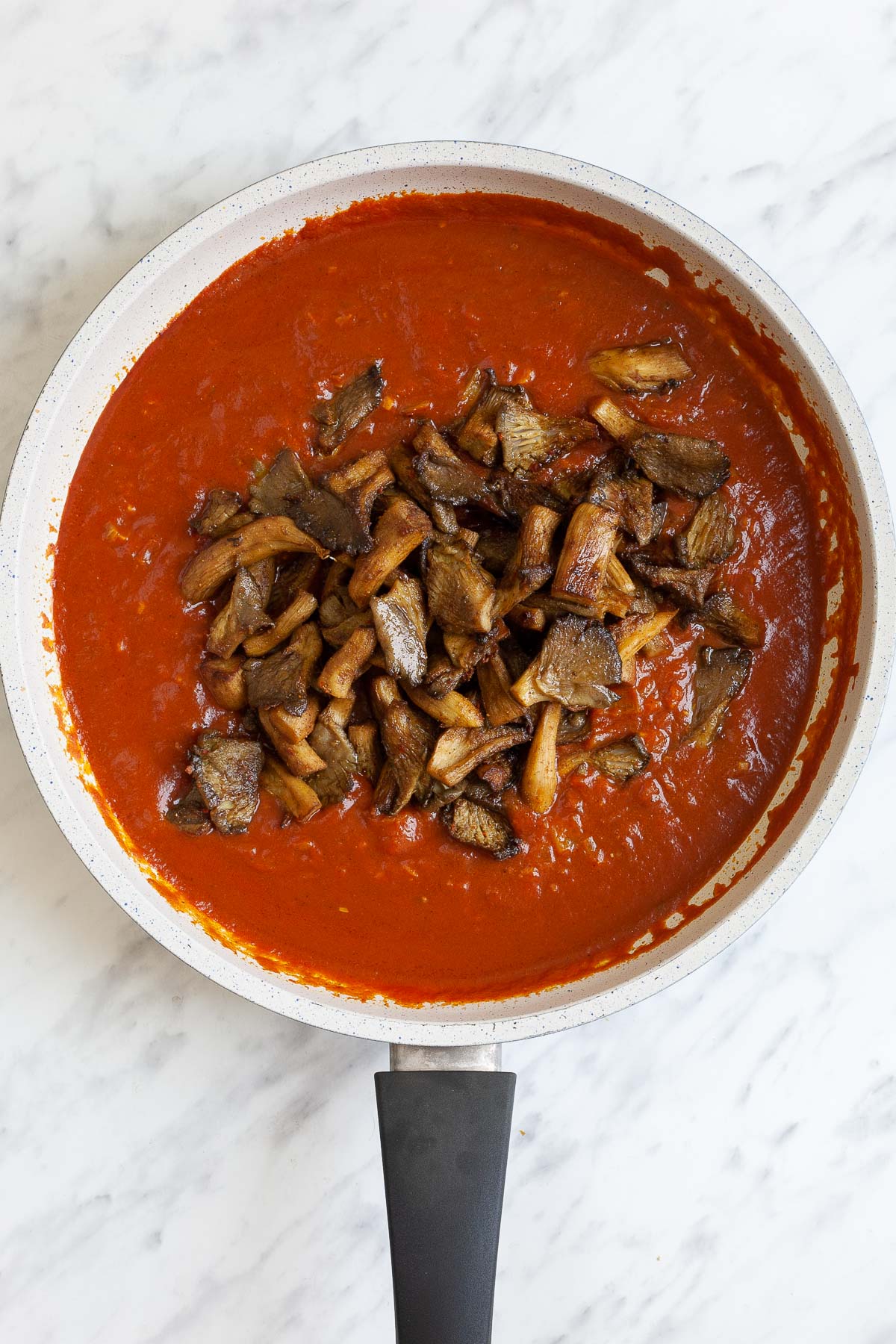 White frying pan with red sauce and brown crispy mushroom strips