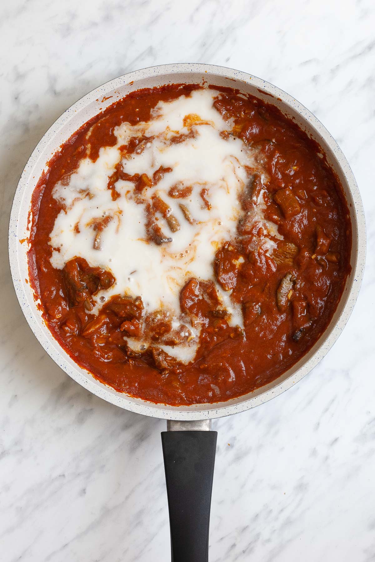 White frying pan with red sauce and brown crispy mushroom strips. A bit of white sauce is added.
