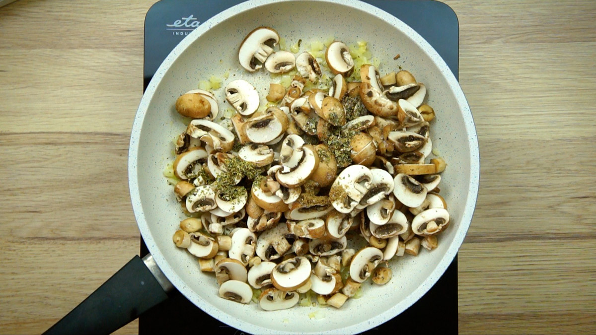 White frying pan with raw mushroom slices and green herbs.