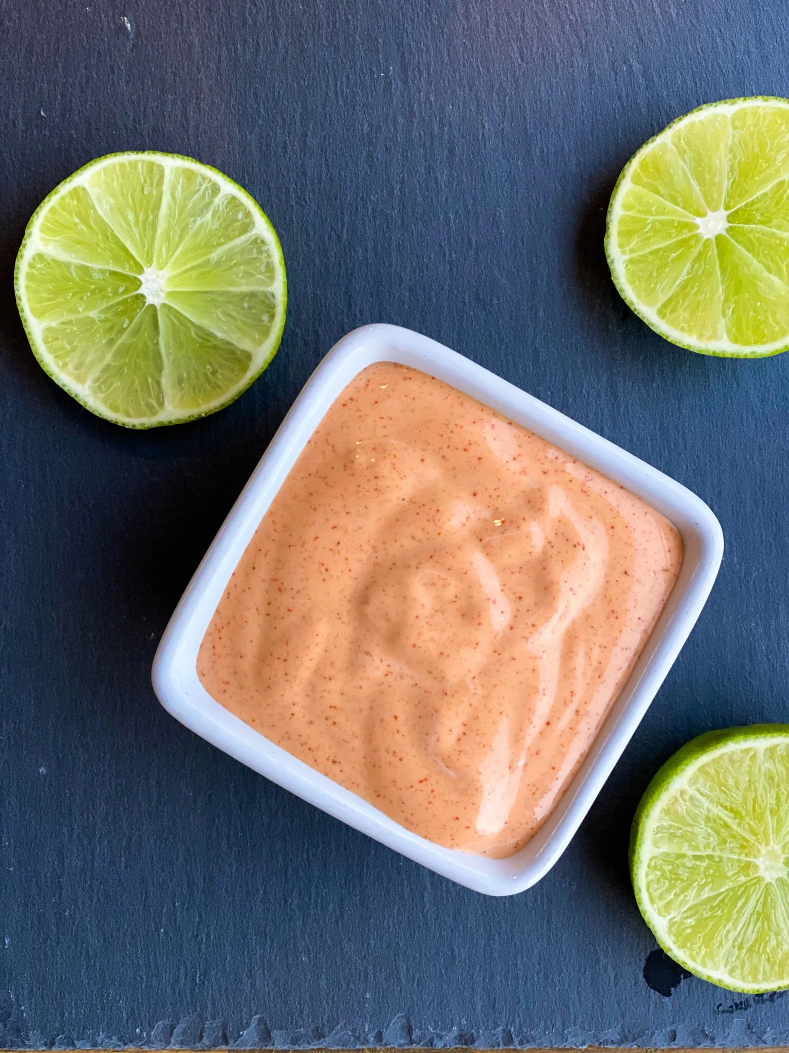 An orange creamy sauce in a small white bowl surrounded by lime slices.