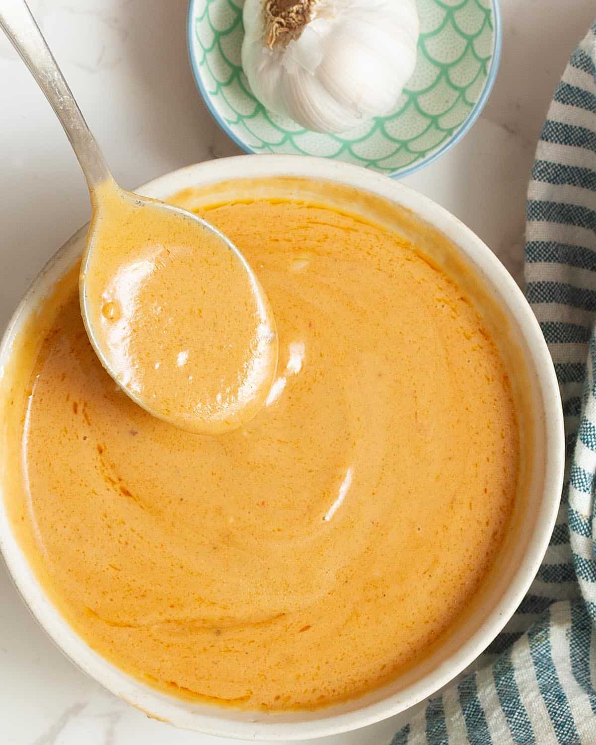 Creamy peanut colored sauce in a white bowl. A spoon is dipped to show the creamy consistenxtr.